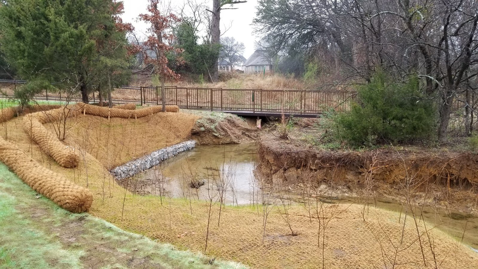 Coir logs and gabion baskets protecting a creek edge beside a footbridge