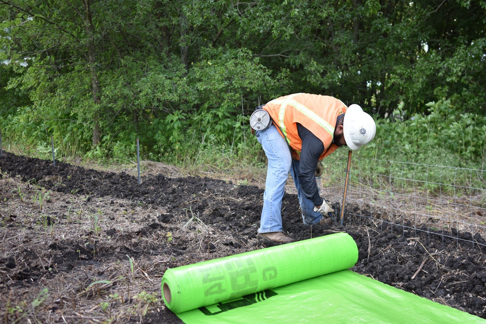 Crew in high-visibility gear rolling out erosion control fabric on a slope