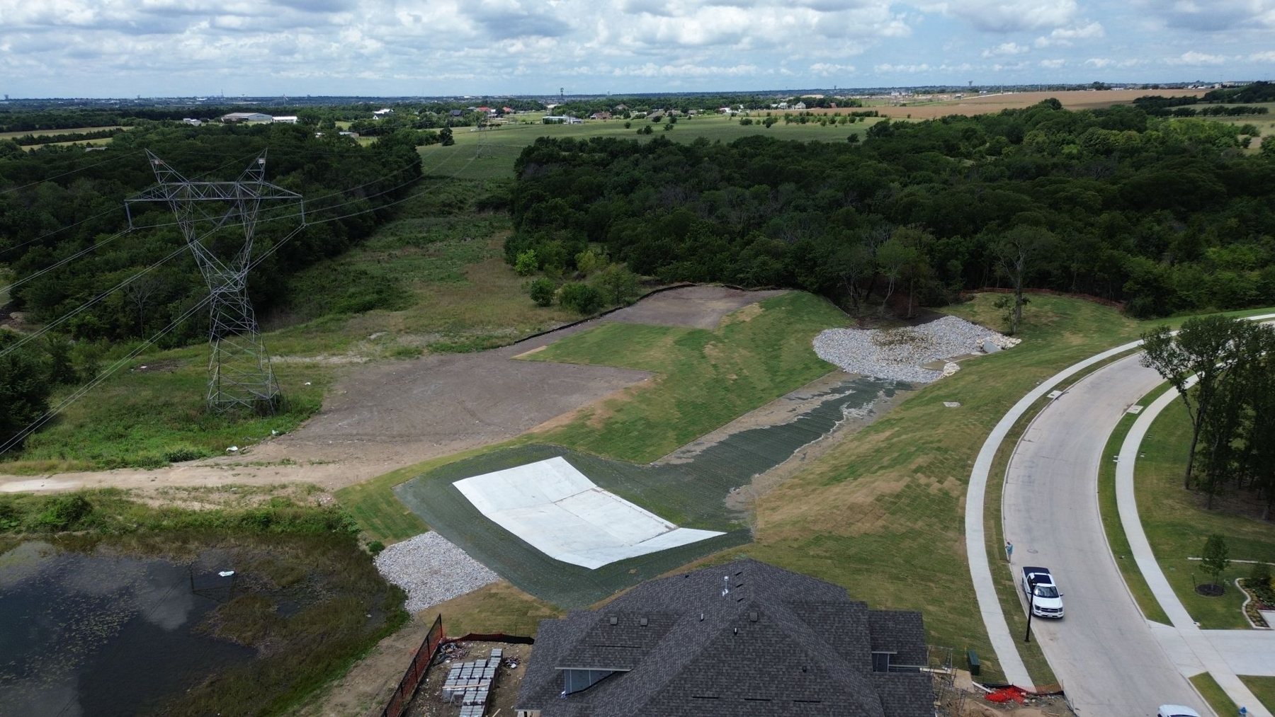Pyramat 75 high-performance turf reinforcement mat lining a pond overflow channel — fresh sod above, riprap at the stormwater discharge