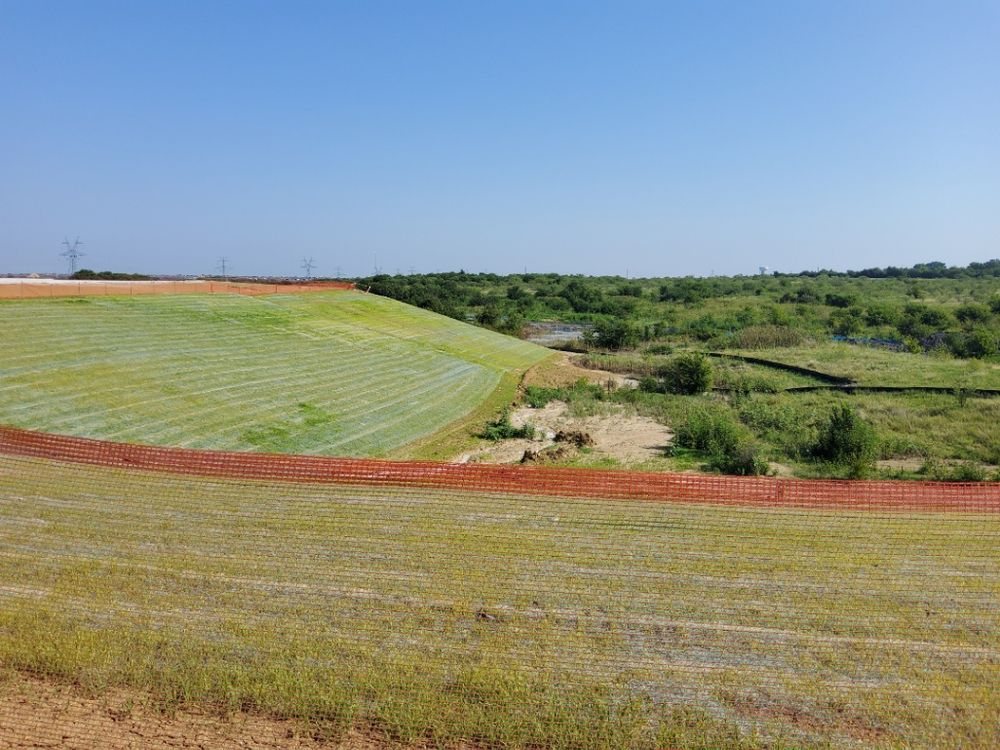 Hydromulched slopes behind safety fencing across a Grand Prairie development