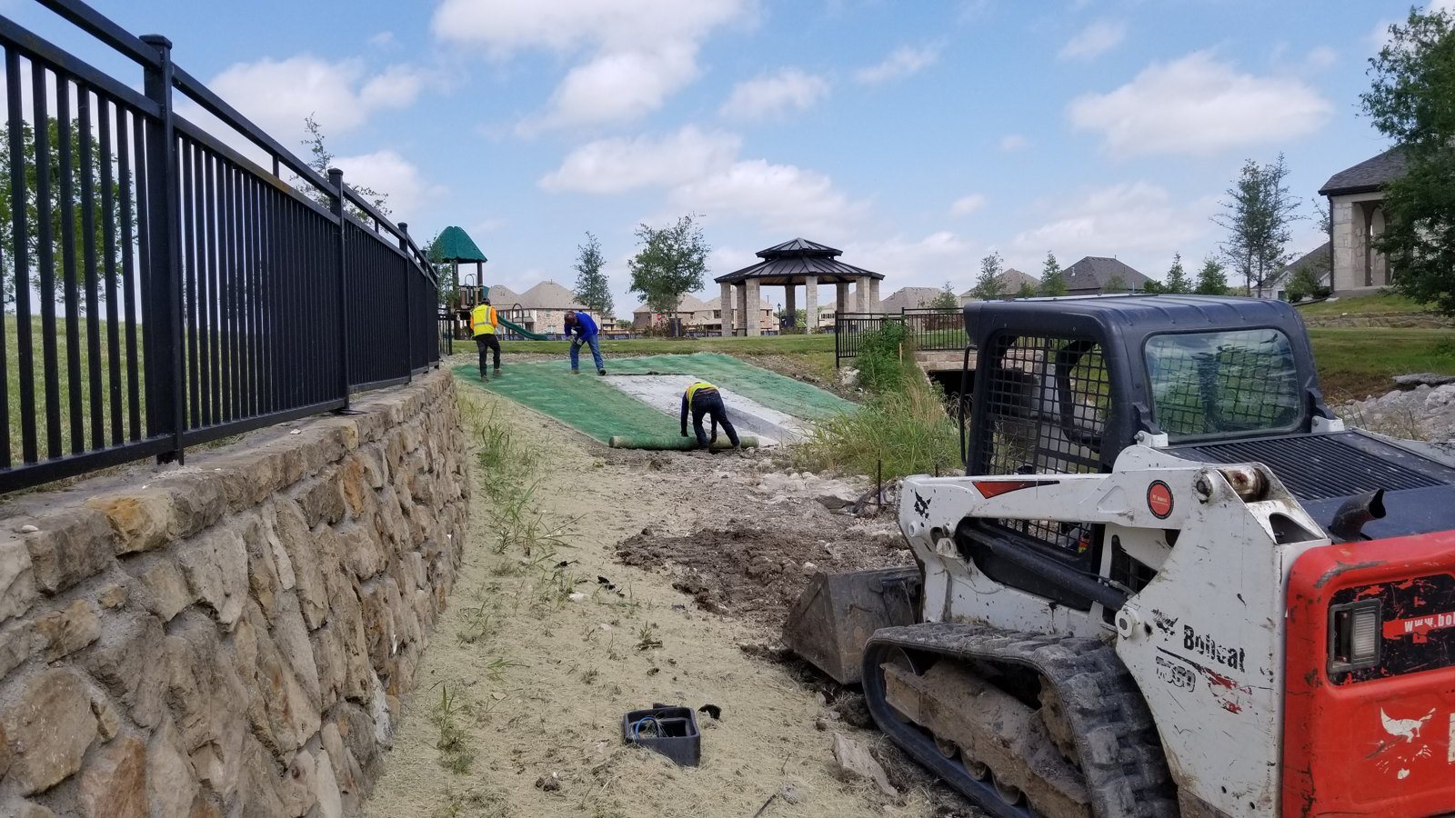 Compact track loader and crew working beside a stone retaining wall