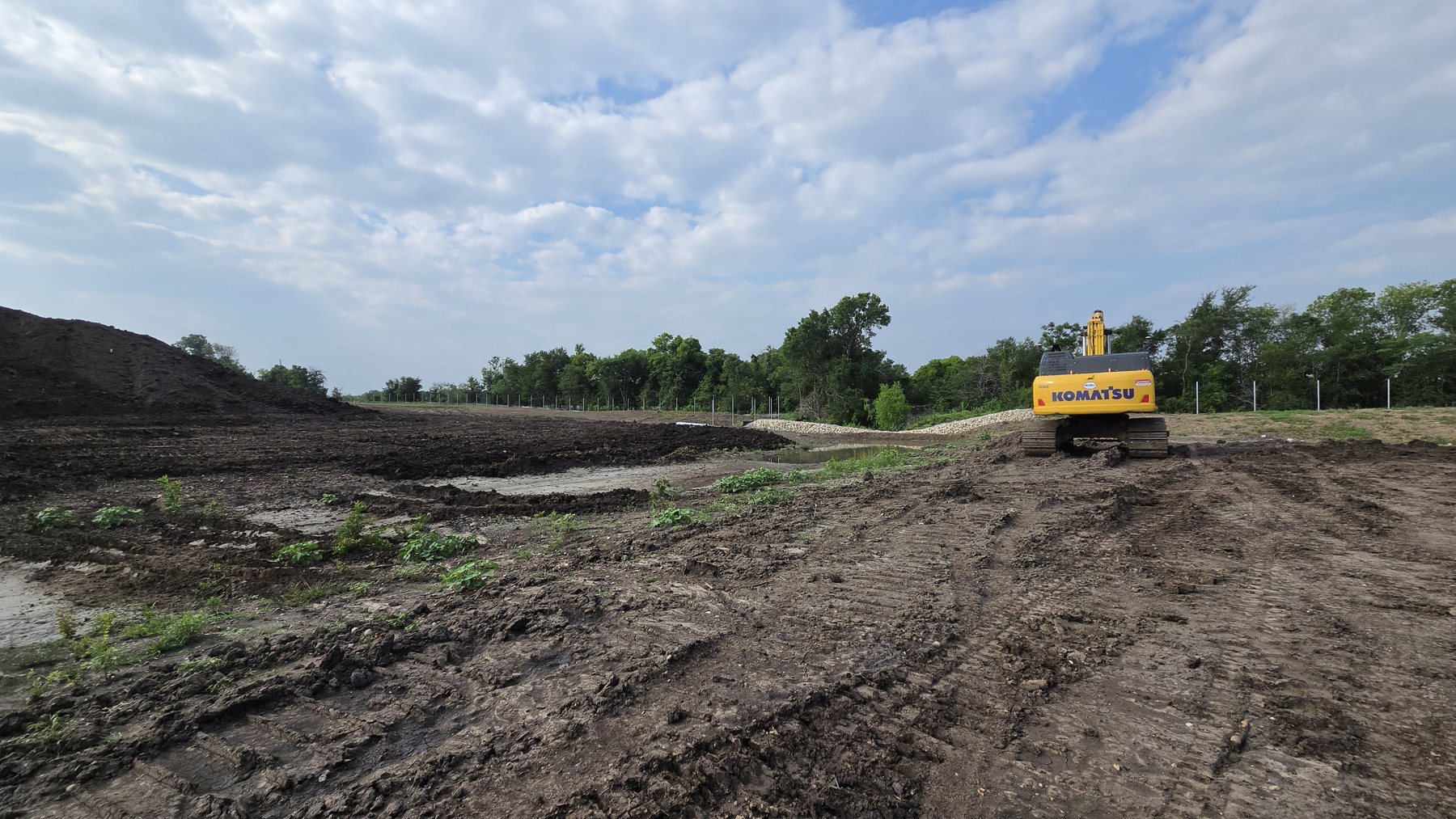 Excavator opening up a mass-grading site with perimeter controls along the tree line